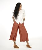 model in a wide leg nutmeg color pant with an apron style panel overlay, worn with a white button up top with 3/4 sleeves and a round neckline