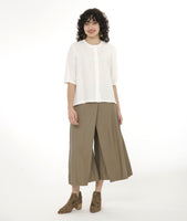 model in a wide leg pebble pant with an apron style panel overlay, worn with a white button up top with 3/4 sleeves and a round neckline