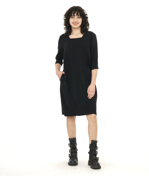 model in a black knee length shift dress with 3/4 sleeves, a squared neckline and pockets set in to the side seams