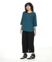model in a wide leg black pant with a teal pull over top with 3/4 sleeves, a round neckline, and a rounded high low hem with a full flowy body in the back