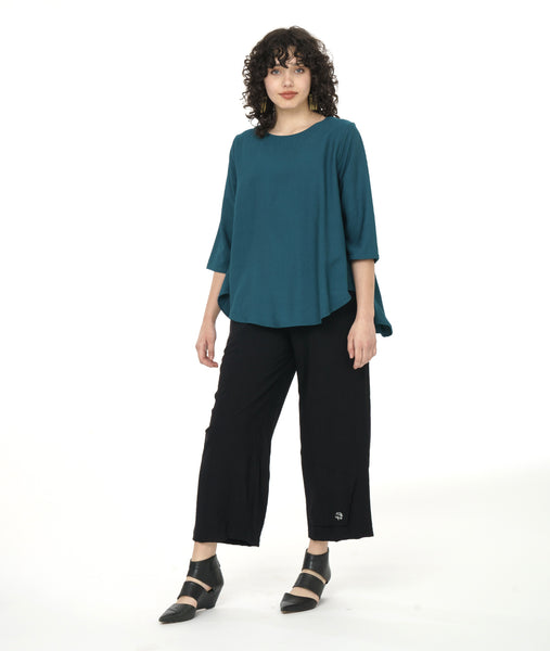 model wearing a teal top with black pants both with button detail in front of a white background