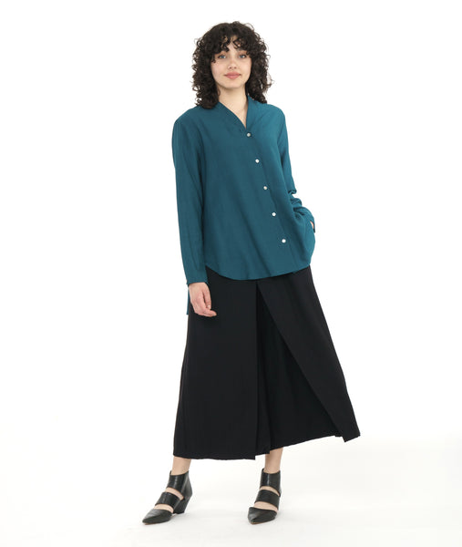 model in a wide leg black pant with a teal button down blouse with long sleeves, a button cuff, a standing collar, and a curved high-low hem 