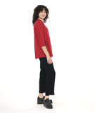 model in a black slim cut pant with a center front seam and split at the ankle, worn with a crimson button down with dips on either hem