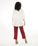 model in a slim cut brick color pant, with an oversize white pullover top with dropped shoulders, a large cowl neck, and elbow length sleeves