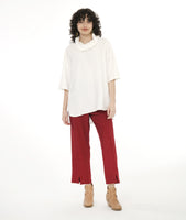 model in a slim cut brick color pant, with an oversize white pullover top with dropped shoulders, a large cowl neck, and elbow length sleeves