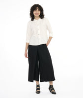 model in a wide leg black pant with a boxy white button down top with a twin button detail along the front, back and sleeve cuffs