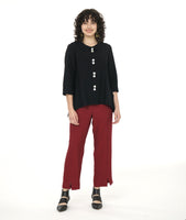 model in a brick red slim cut pant with a center front seam and split at the ankle, worn with a black button down with dips on either hem