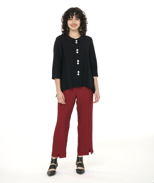 model in a brick red slim cut pant with a center front seam and split at the ankle, worn with a black button down with dips on either hem