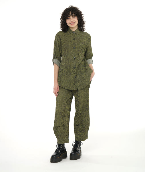 model in a wide leg green and black striped pant with a tulip shape at the ankle, created with tucks. worn with a matching button down blouse with a long rounded hem and rolled and buttoned sleeves