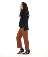 model in a slim rust color pant, worn with a boxy long sleeve black top with splits at the sides and center front. hem is longer in the back. 