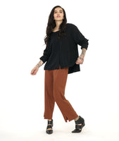 model in a slim rust color pant, worn with a boxy long sleeve black top with splits at the sides and center front. hem is longer in the back. 