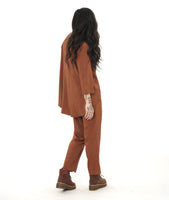 model in a slim rust color pant with a matching flowy pull over top. Top has 3/4 sleeves, a round neckline and a rounded hem with a high-low shape