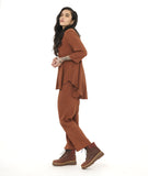 model in a slim rust color pant with a matching flowy pull over top. Top has 3/4 sleeves, a round neckline and a rounded hem with a high-low shape