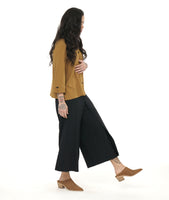 model in a wide leg black pant with an overlay panel on the front legs, worn with an ochre yellow button down blouse with a twin button detail on the front placket, back pleat and sleeve cuffs