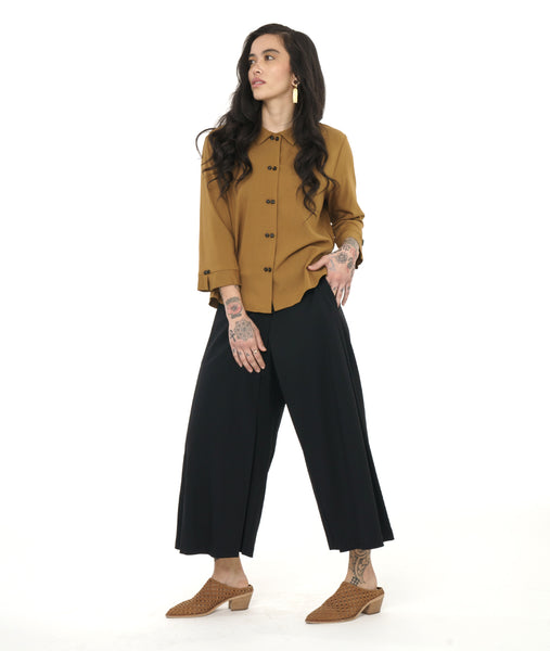 model in a wide leg black pant with an overlay panel on the front legs, worn with an ochre yellow button down blouse with a twin button detail on the front placket, back pleat and sleeve cuffs