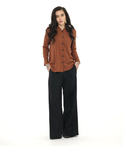 model in a wide leg black palazzo pant, worn with a rust color button down blouse with a round, standing collar and long sleeves