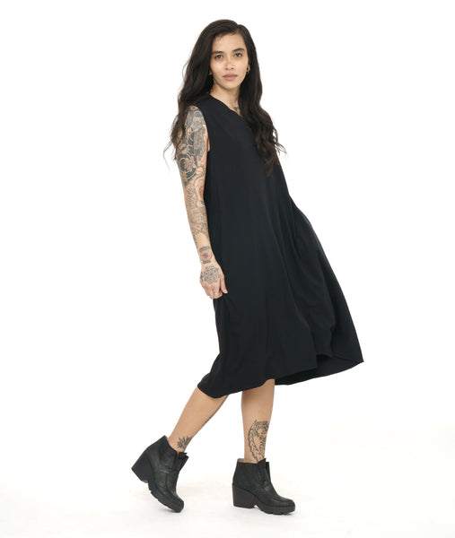 model in a black sleeveless dress with a v neck and center seam. hem is just below the knee, a-line silhouette with pockets at the hip side seams