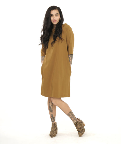 model in an ochre yellow shift dress with elbow length sleeves, a short standing collar, and pockets set in the side seams
