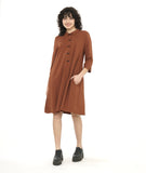 model in a rust color shirt dress with elbow length sleeves and black twin buttons half way down the dress front center