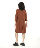 model in a rust color shirt dress with elbow length sleeves and black twin buttons half way down the dress front center