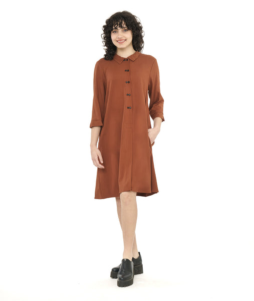model in a rust color shirt dress with elbow length sleeves and black twin buttons half way down the dress front center