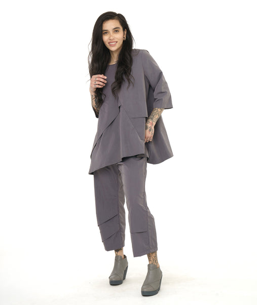 model in a boxy grey top with long dolman sleeves, a standing cowl neck, and a matching slim pant with asymmetrical seams along either leg