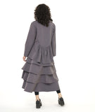 model in a grey button down blouse with a pleated drape in the back, worn with black leggings and a long tiered skirt in a matching fabric