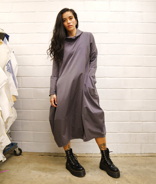 model in a grey dress with a large cowl neck, long sleeves, and oversized hip pockets. 
