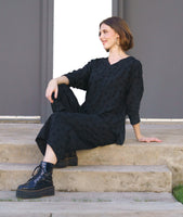 model in a black wide leg pant with a matching pullover top with a v-neck and long sleeves. fabric has a textured circle print