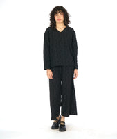 model in a black wide leg pant with a matching pullover top with a v-neck and long sleeves. fabric has a textured circle print