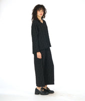 model in a black boxy pullover top with a v-neck and long sleeves, worn with a matching black wide leg pant. fabric has a pinched circle texture