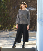 model in a boxy green pullover top with long sleeves and a matching black wide leg pant. fabric has a pinched circle texture