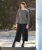 model in a boxy green pullover top with long sleeves and a matching black wide leg pant. fabric has a pinched circle texture