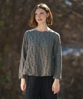 model in a boxy green pullover top with long sleeves and a matching wide leg black pant. fabric has a pinched circle texture