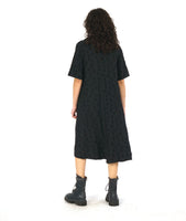 model in a black dress with 3/4 raglan sleeves, a short cowl neckline, and a flowy skirt hitting just below the knee. Dress has a textured circle design all over 