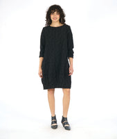 model in a black shift dress with long sleeves and curved princess seams with pockets set in at the hips. fabric is black with a pinched circle texture