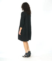 model in a black shift dress with long sleeves and curved princess seams with pockets set in at the hips. fabric is black with a pinched circle texture