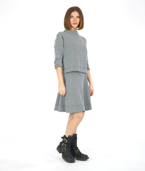 model in a black and white zipper print paneled knee length skirt, worn with a matching pullover top with a dropped shoulder and a high neckline