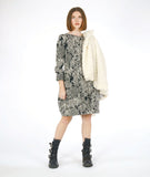 MODEL IN A BLACK AND WHITE LACE PRINT SHIFT DRESS WITH LONG SLEEVES AND A KNEE LENGTH HEM, HOLDING A WHITE FAUX FUR COAT