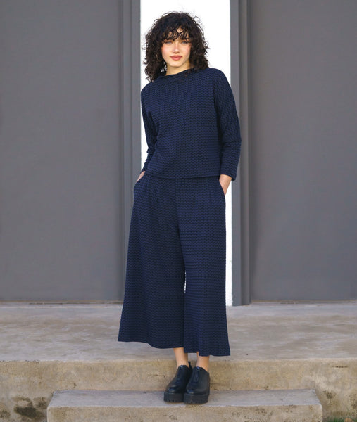 model in a black and blue zipper print paneled wide leg pant, worn with a matching pullover top with a dropped shoulder and a high neckline