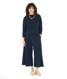 model in a black and blue zipper print paneled wide leg pant, worn with a matching pullover top with a dropped shoulder and a high neckline