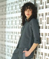 model in a black and white grid print blouse with 3/4 sleeves and a twin button detail, worn with a matching pant with a contrasting tuxedo stripe