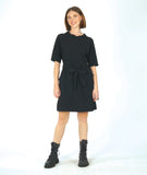 model in a textured black shift dress with a matching tie belt, deep exterior pockets, and elbow length raglan sleeves