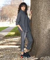 model in a black and white grid print top with an overlapping cowl neck and 3/4 sleeves, worn with a matching slim cut pant with a contrasting tuxedo stripe. model is standing next to a tree