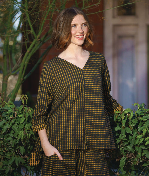 model in a black and yellow wide leg pant with a tapered ankle and oversized exterior pockets, worn with a matching pullover top with rolled long sleeves, a n-neck and the bodice split in to contrasting stripe directions