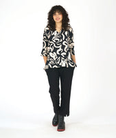 model in a black pullover blouse with an ivory floral print and 3/4 sleeves, a vneck, and a split at the front center seam. worn with a straight leg black pant