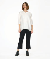 model in a slim black pant with a white 3/4 sleeve tunic with a rounded neckline with a v-split in the front center. top as a high-low hem