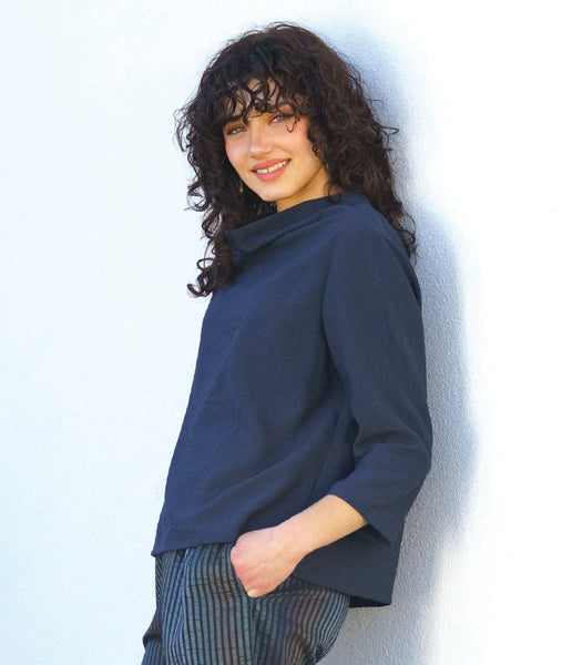 model in a navy blue cowl pullover top with 3/4 sleeves and a striped pant