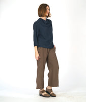 model in a straight leg brown pant with a navy blue pullover top with 3/4 sleeves and a cowl neck