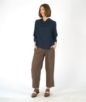 model in a straight leg brown pant with a navy blue pullover top with 3/4 sleeves and a cowl neck